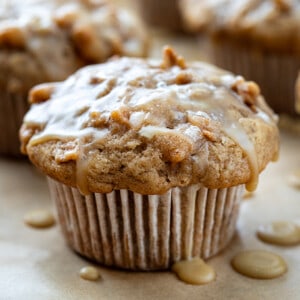 Apple Muffin on Parchment Paper with Maple Glaze Dripping Over the Muffin and Pooling on the Paper.