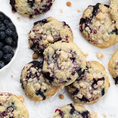 Blueberry Crumble Cake Cookies on White Parchment Next to Fresh Blueberries.