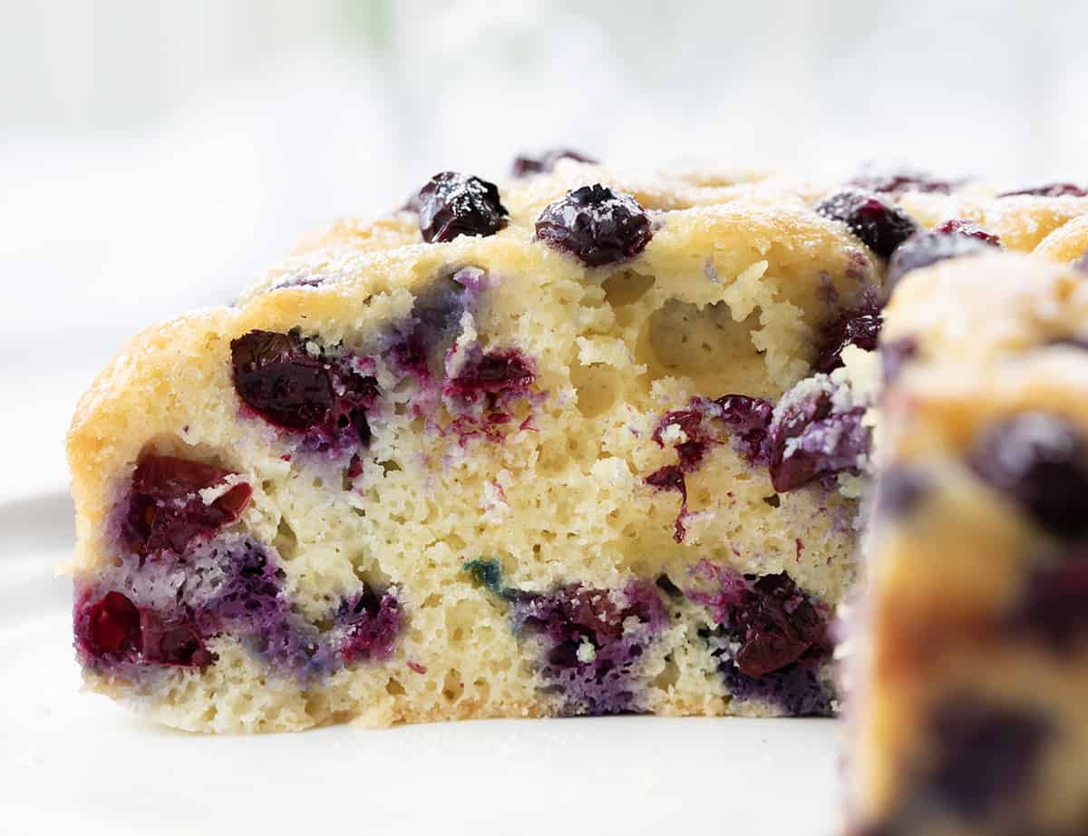Blueberry Breakfast Cake is loaded with fresh blueberries, baked, and poked with holes to be saturated with a warm sugary milk mixture for a super moist and rich cake. Then, it's dusted with confectioners' sugar. This type of cake, known as a poke cake, is the perfect way to add flavor and extra moisture to each bite. And, don't save this cake just for breakfast; it is also a delicious snack or dessert. Close up of the inside of a Blueberry Breakfast Cake.