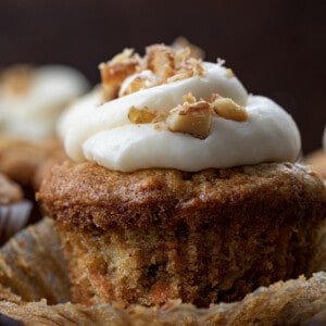 Close up of a Carrot Cake Cupcake with Wrapper Peeled Back and Candied Walnuts on Top of the Cream Cheese Frosting.