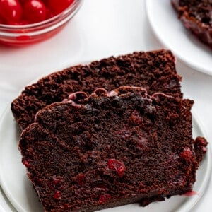 Close up of Cherry Brownie Bread Slices on a Plate with Cherries in the Background.