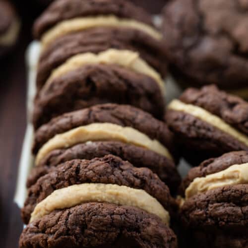 Rows of Chocolate Peanut Butter Sandwich Cookies in a Dish on a Dark Cutting Board.