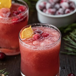 Glass of Christmas Slush with an Orange Garnish and Sugared Cranberries.