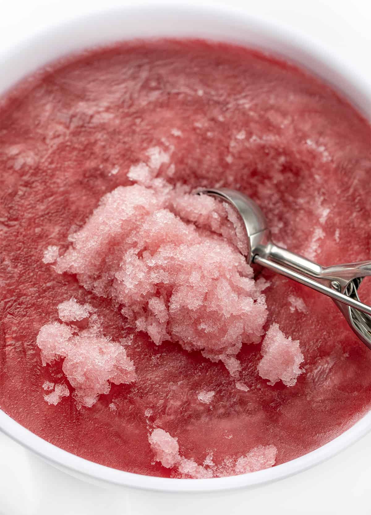 Ince Cream Scoop Scooping up Slush form Container of Cranberry Slush.