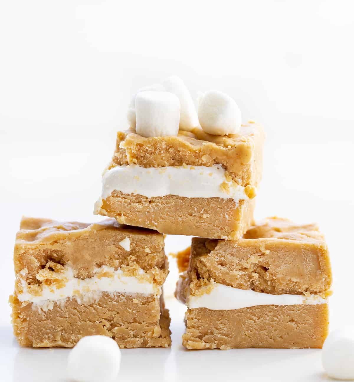 This fudge was inspired by a fluffernutter sandwich, which is a sandwich made with peanut butter and marshmallow fluff. Fluffernutter Fudge is two layers of melted peanut butter and white chocolate with a layer of marshmallow fluff in between. If you love peanut butter, do not miss out on this recipe! Pieces of Fluffernutter Fudge or Peanut Butter and Marshmallow Fudge Stacked in a Pyramid on a White Counter.