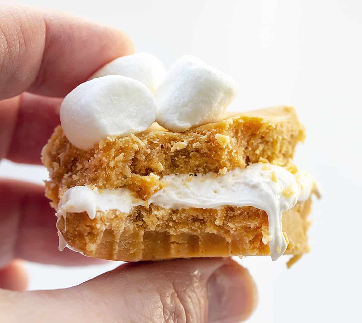 This fudge was inspired by a fluffernutter sandwich, which is a sandwich made with peanut butter and marshmallow fluff. Fluffernutter Fudge is two layers of melted peanut butter and white chocolate with a layer of marshmallow fluff in between. If you love peanut butter, do not miss out on this recipe! Hand Holding a Piece of Fluffernutter Fudge that has a Bite Taken out of it.
