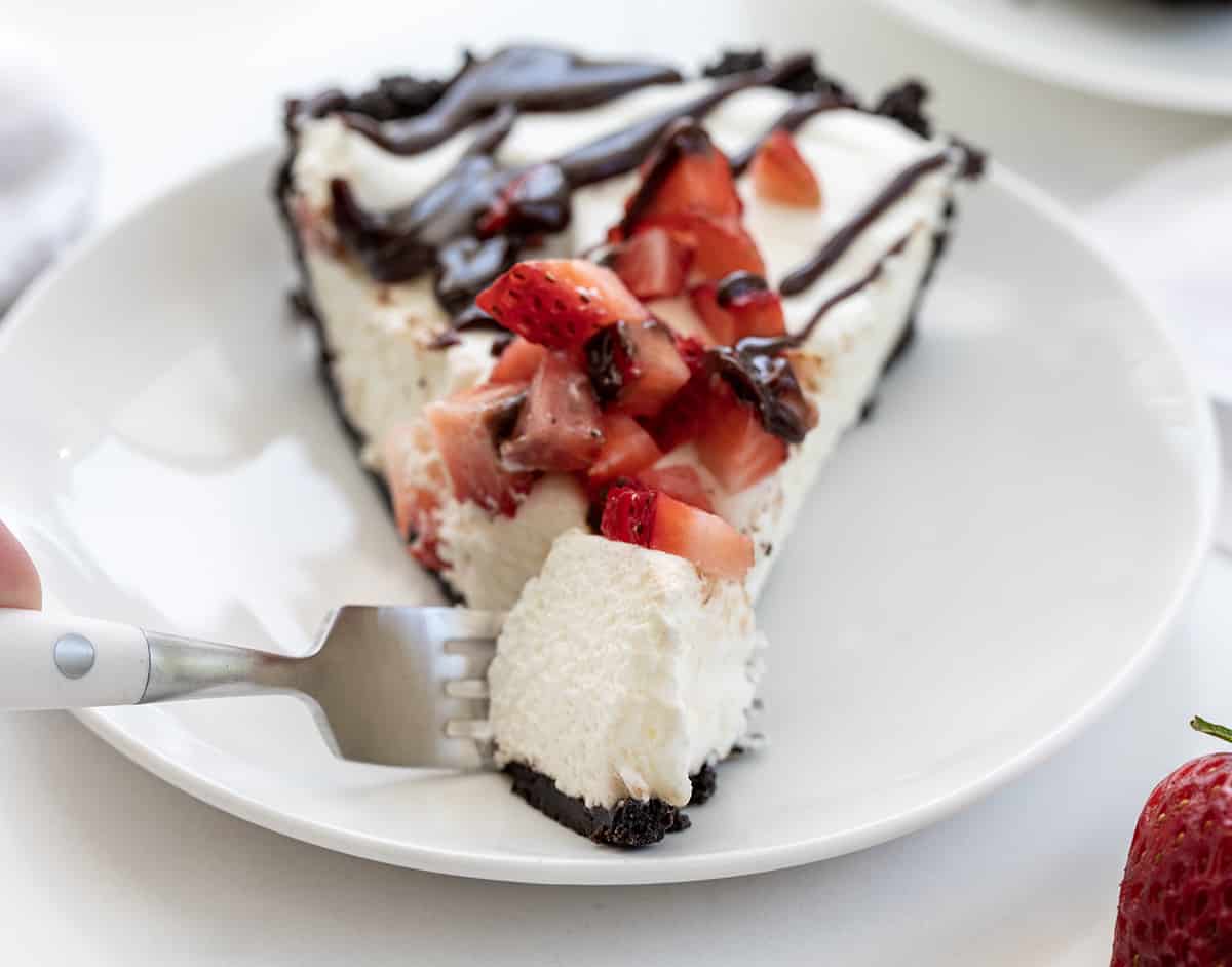 Fork Taking a Bite of Chocolate Strawberry Marshmallow Pie off a White Plate.