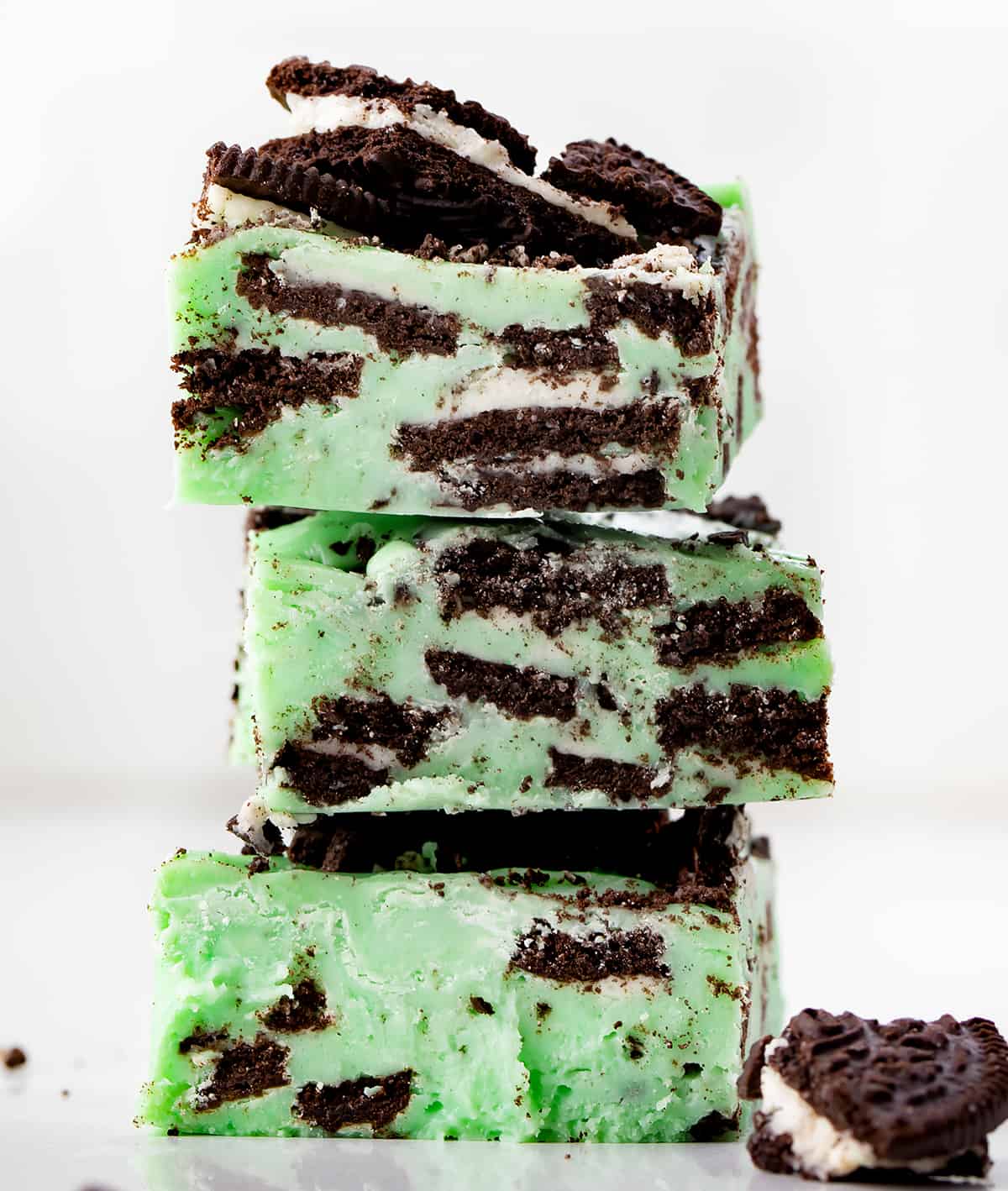 Creamy, no-fuss Mint Chocolate Oreo Fudge needs to be the next recipe on your dessert line-up. This delicious mint and chocolate cookie treat will have your guests coming back for seconds and thirds. Stack of Mint Oreo Fudge Pieces on a White Counter.