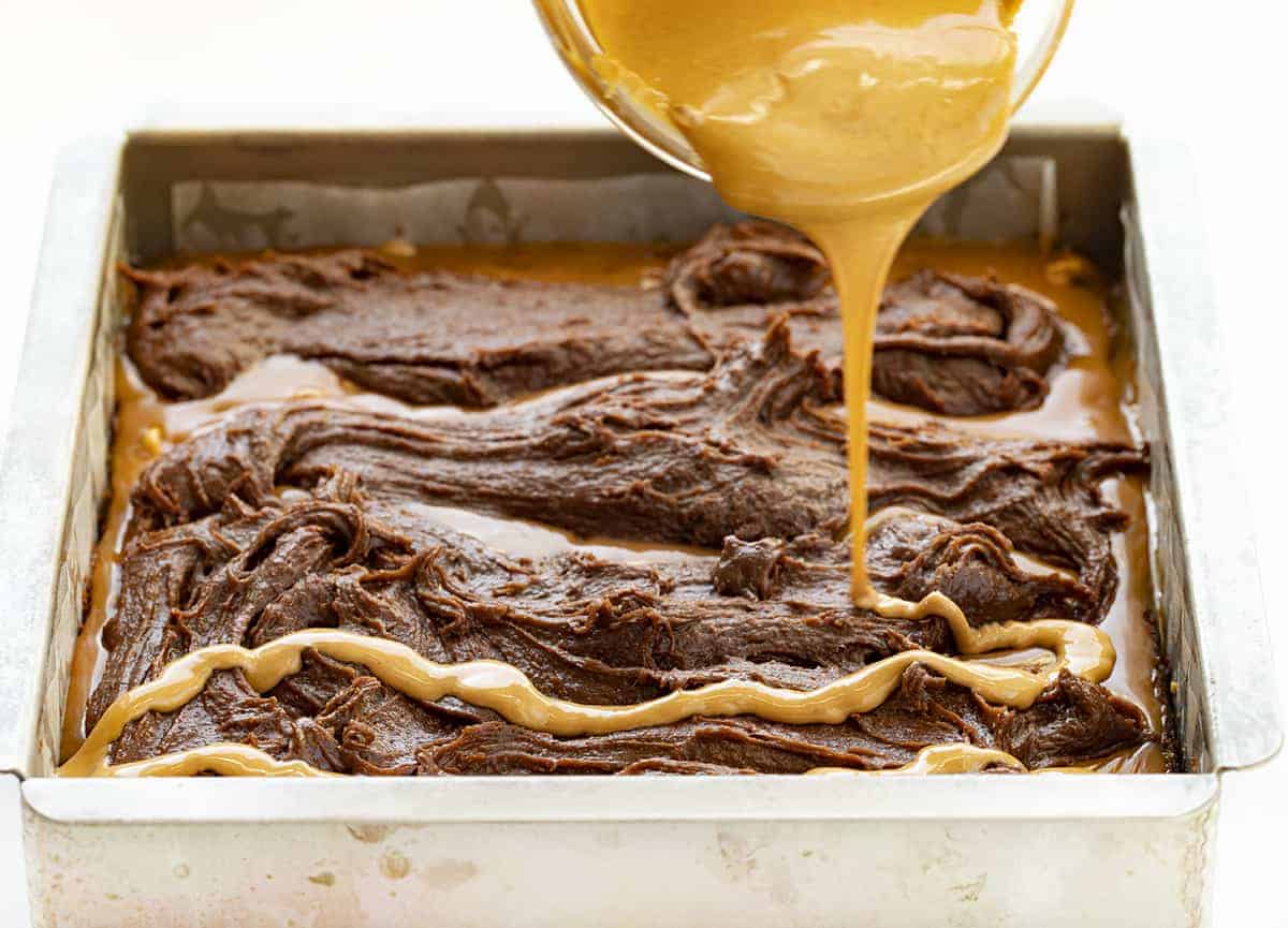 Peanut Butter Brownie Caramelitas are the ULTIMATE ooey gooey brownie! They have a sweet caramel center, along with a layer of peanut butter morsels with more peanut butter drizzled on top. Baking, Brownies, Brownie Recipe, Dessert, Peanut Butter Dessert, Caramel Dessert, dessert recipes, decadent desserts, ooey gooey desserts, i am baker, iambaker Pouring Melted Peanut Butter Over Brownie Batter for Peanut Butter Brownie Carmelitas
