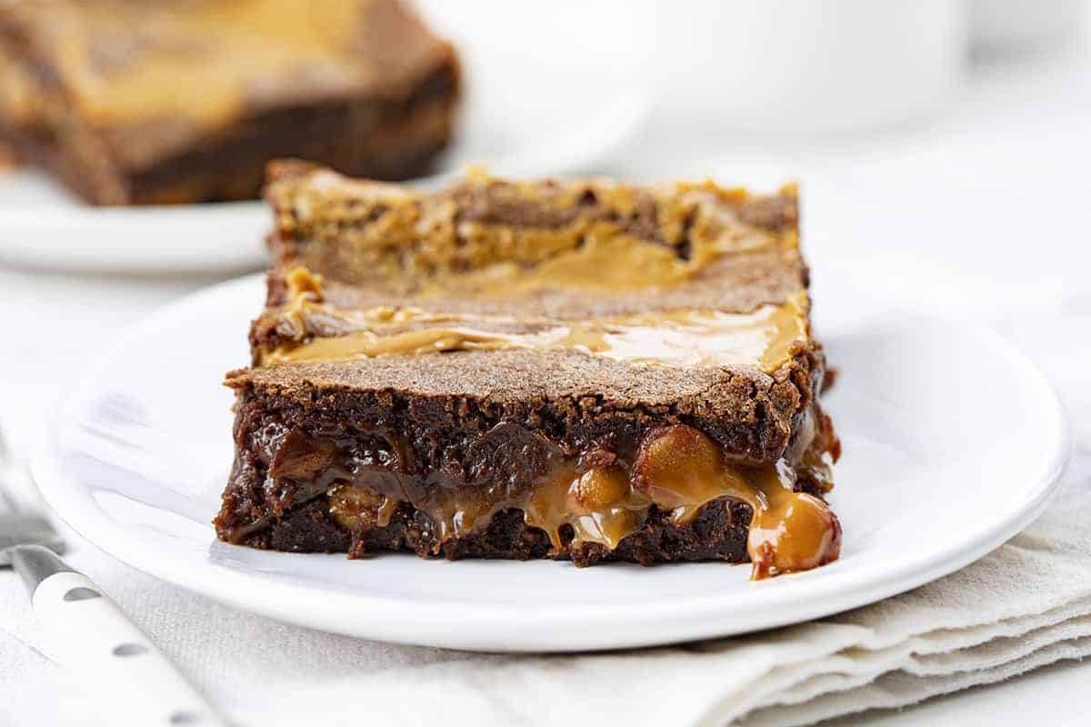 Peanut Butter Brownie Caramelitas are the ULTIMATE ooey gooey brownie! They have a sweet caramel center, along with a layer of peanut butter morsels with more peanut butter drizzled on top. Baking, Brownies, Brownie Recipe, Dessert, Peanut Butter Dessert, Caramel Dessert, dessert recipes, decadent desserts, ooey gooey desserts, i am baker, iambaker Peanut Butter Brownie Carmelita on a Plate