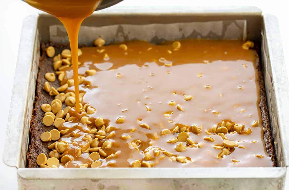 Peanut Butter Brownie Caramelitas are the ULTIMATE ooey gooey brownie! They have a sweet caramel center, along with a layer of peanut butter morsels with more peanut butter drizzled on top. Baking, Brownies, Brownie Recipe, Dessert, Peanut Butter Dessert, Caramel Dessert, dessert recipes, decadent desserts, ooey gooey desserts, i am baker, iambaker Drizzling Caramel Over Peanut Butter Morsels and a Baked Brownie