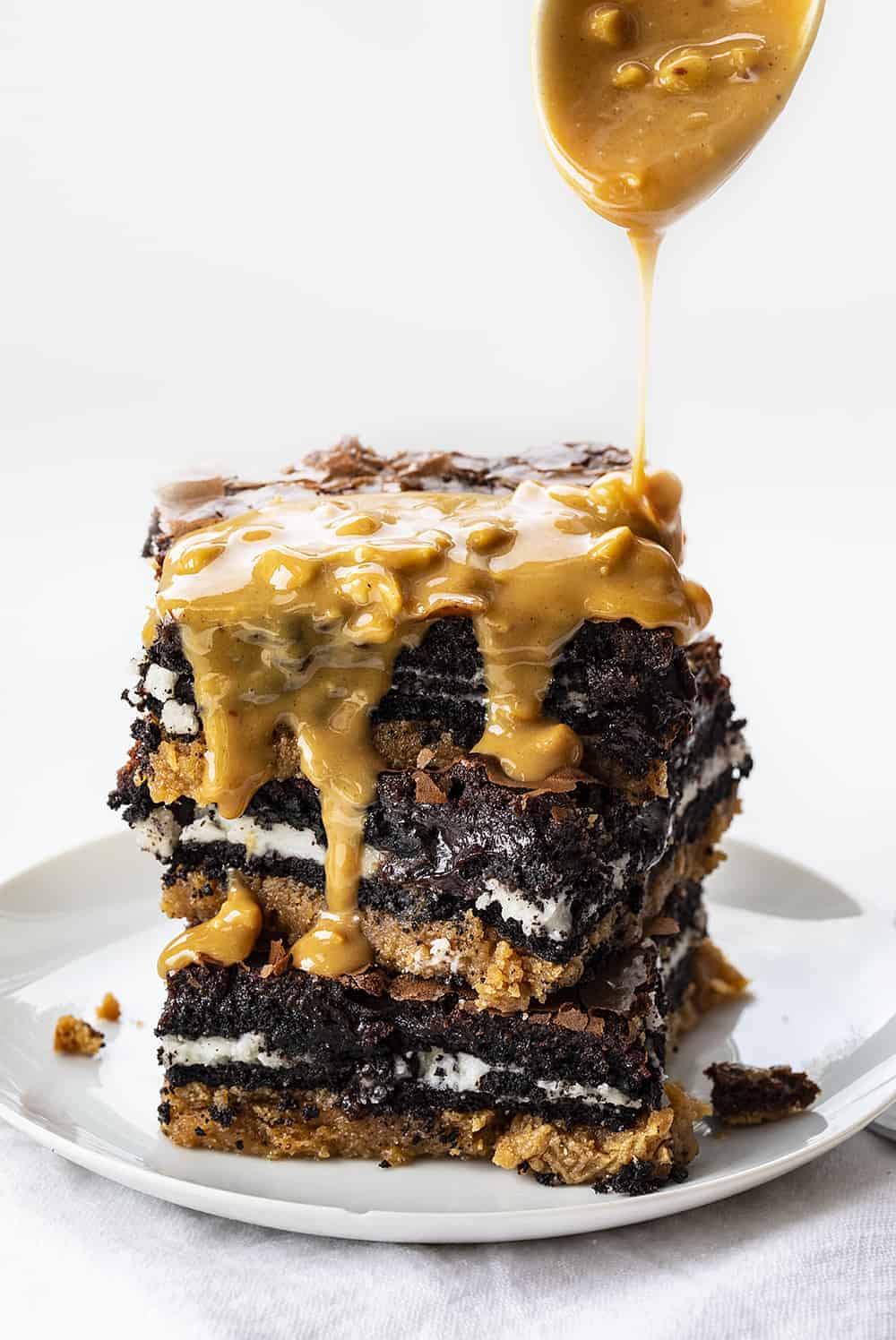 Stack of Peanut Butter Slutty Brownies with Peanut Butter Butterscotch Sauce Being Drizzled Over Top