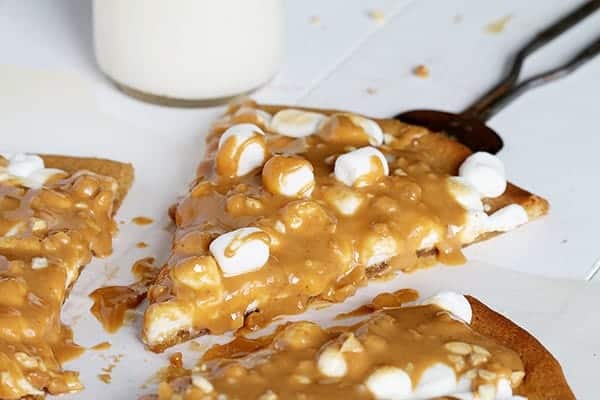 One Slice of Peanut Butter Dessert Pizza Pulled Apart from the Rest with Milk in Background