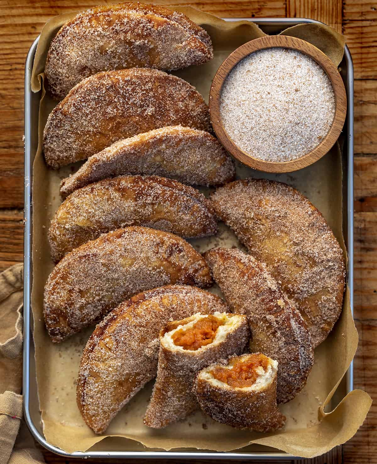 Pan of Pumpkin Hand Pies with One Broken in Half Showing Inside. Pumpkin Hand Pies, Pumpkin Bombs, Pumpkin Desserts, Pumpkin Snacks, Pumpkin Spice, Pumpkin Crisps, Fried Pumpkin Pies, Individual Pumpkin Pies, Cinnamon Sugar Pumpkin Pies, fall recipes, Thanksgiving Recipes, Christmas Recipes, Thanksgiving Desserts, i am baker, iambaker