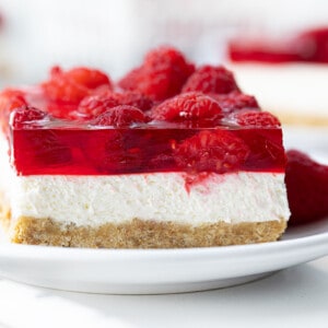 Raspberry Pretzel Salad on a White Plate with Fresh Raspberries Around and More in the Background.