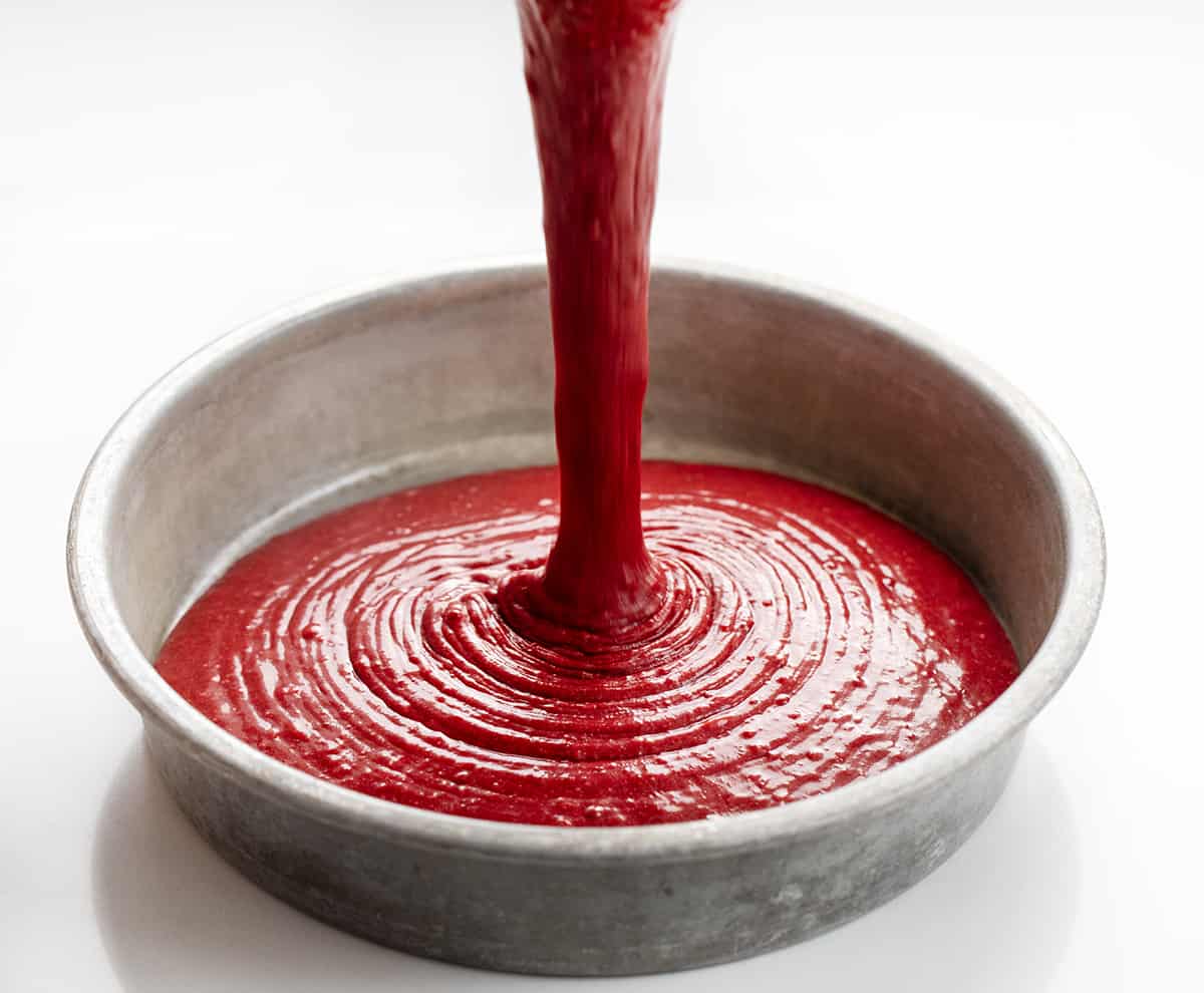 Pouring red velvet cake batter into round baking pan.