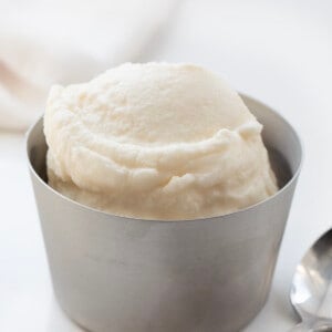 Scoop of Soft Serve Ice Cream in a Metal Bowl on a White Counter with Spoon Nearby.