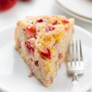 Piece of Fresh Strawberry Cake on a White Plate with Strawberries in the Background.