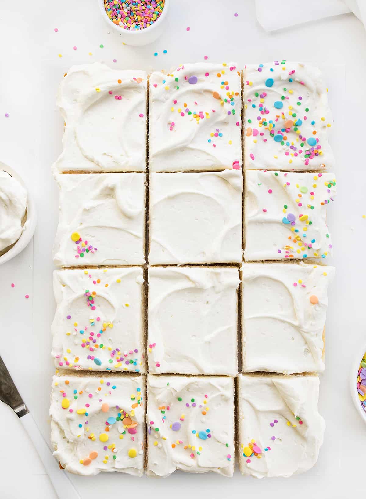 Whole Vanilla-Delight Cake or White Cake on a White Counter with Pastel Sprinkles and Cut Into Pieces.