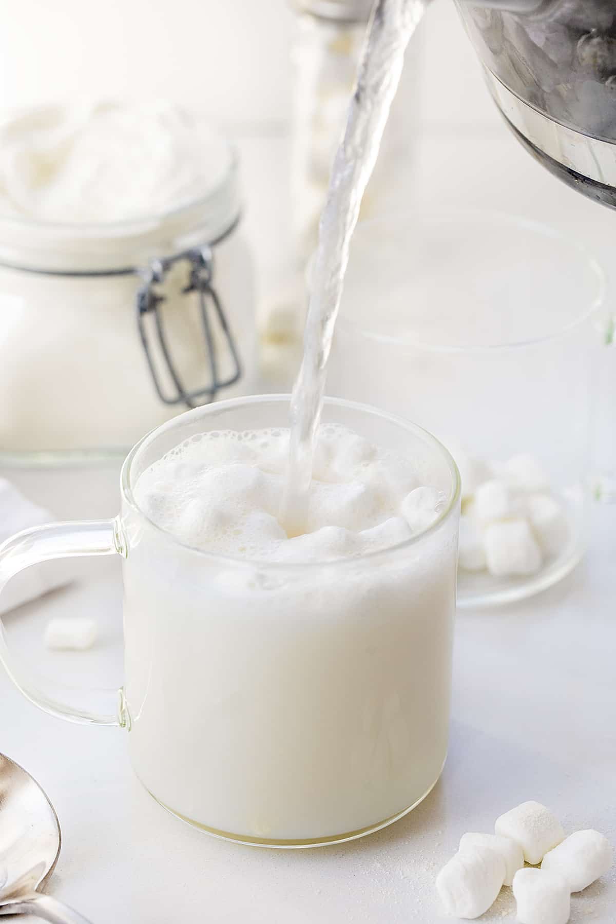 Pouring Hot water over white chocolate hot cocoa mix and mini marshmallows in a clear glass.