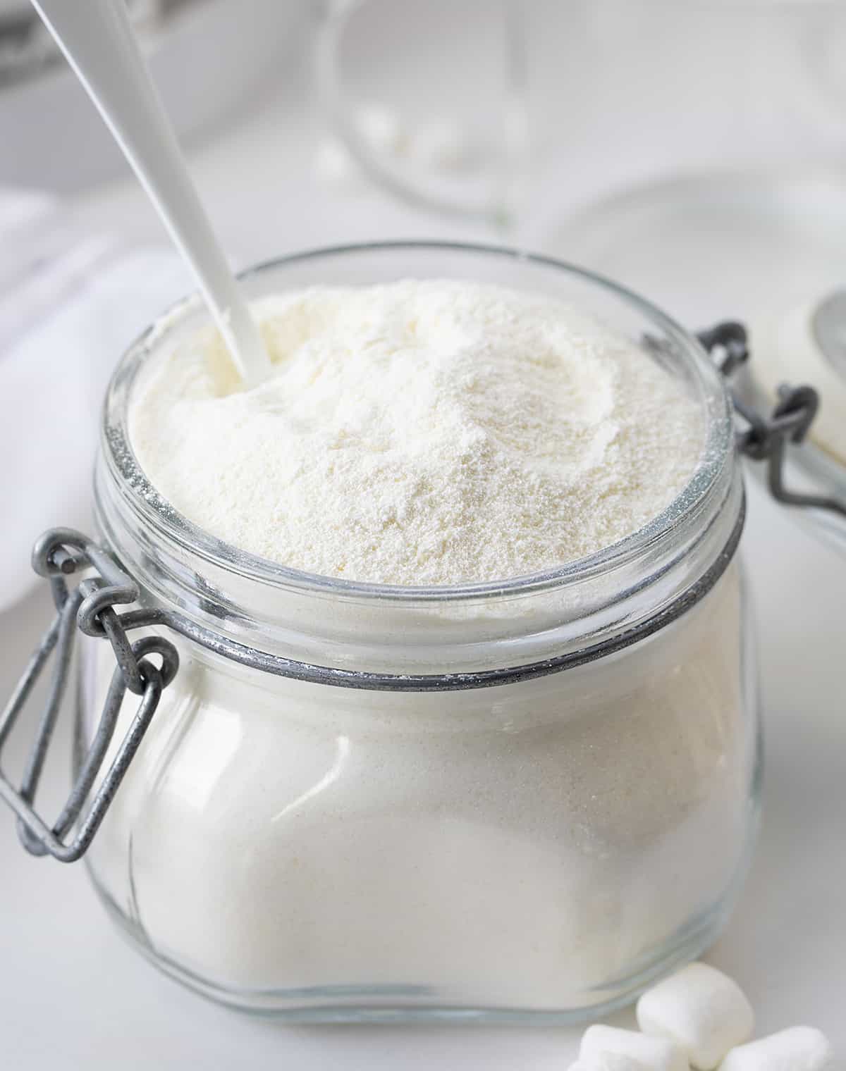 Container filled with homemade white hot chocolate powder and a spoon in it.