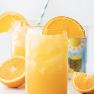 Glasses of Yellow Hammer Slammer with an Orange Garnish on a White Counter.